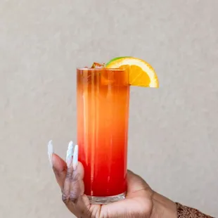 a hand holding a tall glass of orange juice