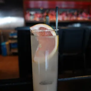 a glass of grapefruit cocktail with a straw and a slice of grapefruit