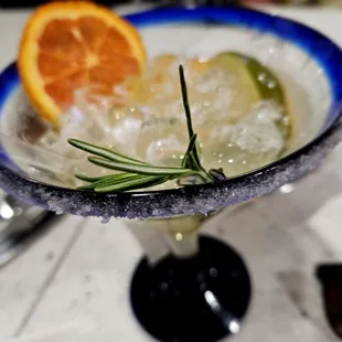 a closeup of a margarita with a slice of orange and rosemary garnish