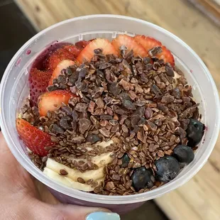 a hand holding a bowl of fruit and granola