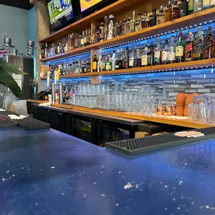 a bar with a blue counter top and shelves of liquor