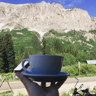 a person holding a coffee cup in front of a mountain