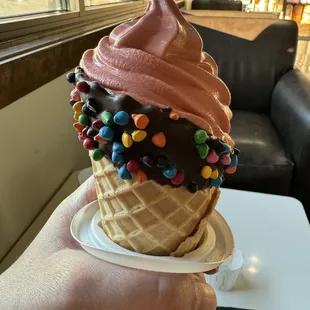 Red velvet soft serve ice cream in waffle cone with chocolate and M&amp;Ms.