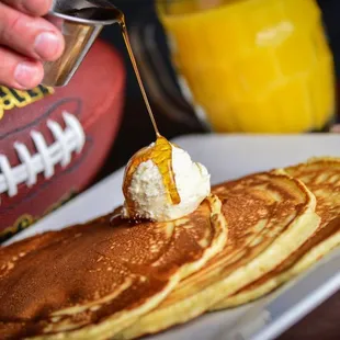 a person pouring syrup onto pancakes