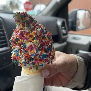 a hand holding an ice cream cone with sprinkles