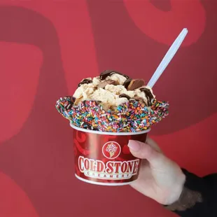 a hand holding a cup of ice cream with sprinkles