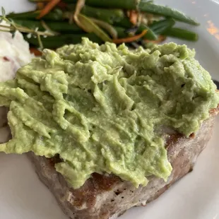 Tuna steak that has guacamole topping with mashed potatoes and veggies