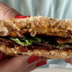 a woman holding a sandwich with bacon and lettuce