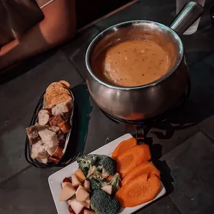 a pot of fondue and a plate of vegetables