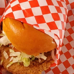  a chicken sandwich wrapped in red and white checkered paper