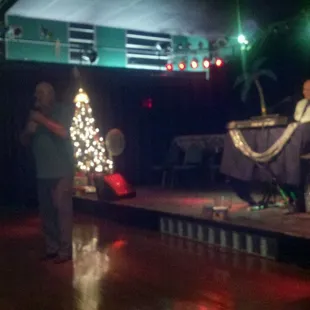 a man standing on a stage with a christmas tree in the background