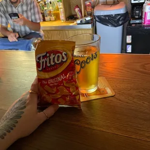 a person holding a bag of chips and a glass of beer