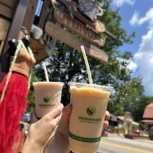 a hand holding two cups of iced coffee