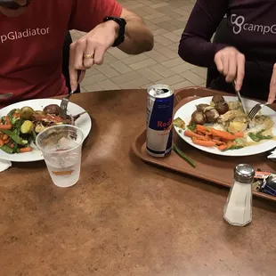 two people sitting at a table with plates of food