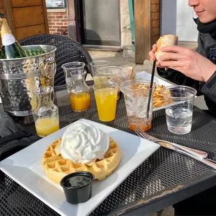a woman eating a waffle with whipped cream and orange juice