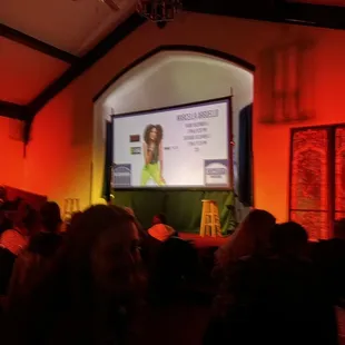 a woman on a screen in a room full of people