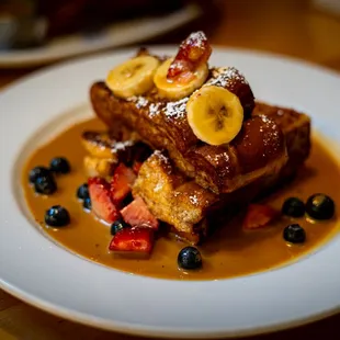 a plate of french toast with bananas, strawberries and blueberries