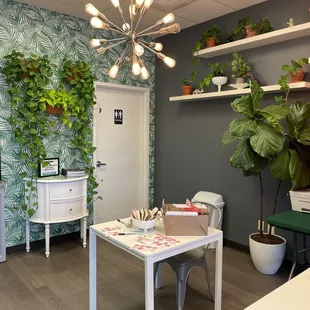 a room with a desk, shelves, and plants