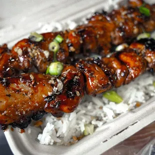a chicken skewer with rice in a styrofoam container