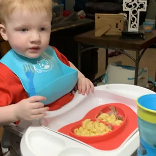 a toddler sitting in a high chair with a bowl of food in front of him