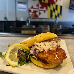 a chicken sandwich with coleslaw and a side of lemon wedges