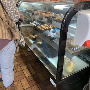 a woman standing in front of a display case of pastries