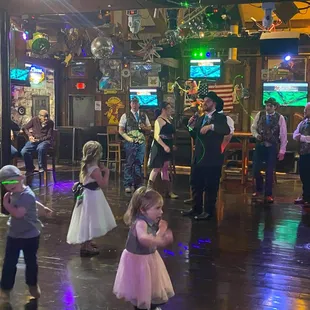 a young girl in a pink dress dancing with other people in the background