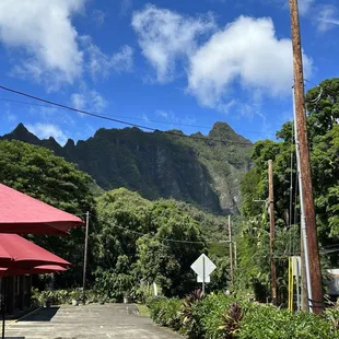 a walkway with tables and umbrellas and mountains in the background