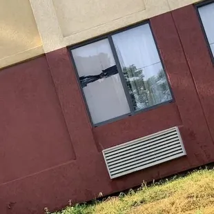 Broken windows on ground floor. Cardboard window, wet from rain.