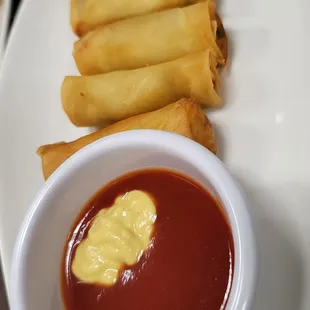a plate of spring rolls and a bowl of ketchup