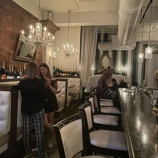 Gorgeous bar and booth seating area with white leather cushioning and black wooden trim. Chandeliers.