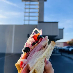 a person holding a sandwich in front of a corti bros sign