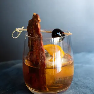 a glass filled with a drink and a slice of bacon