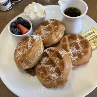 a plate of waffles with powdered sugar and berries