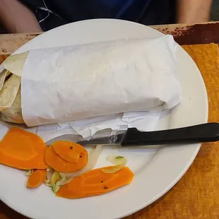 a burrito with carrots and a knife