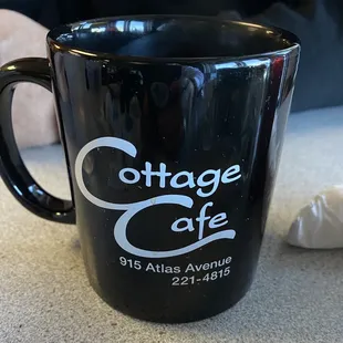 a black coffee mug with the cottage cafe logo on it
