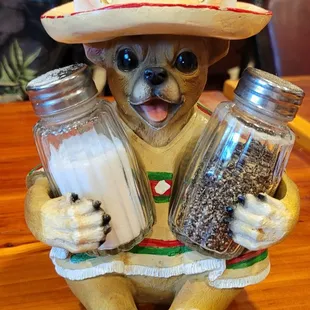 Puppy wearing hat holding salt and pepper shakers.