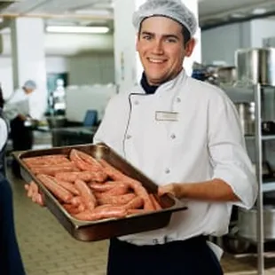 a chef holding a tray of sausages