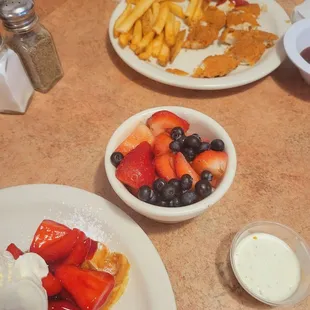Side of fruit and a kids chicken strips and fries.