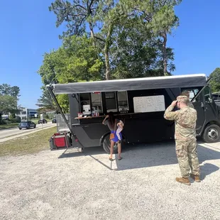 a soldier taking a picture of a little girl standing in front of a food truck