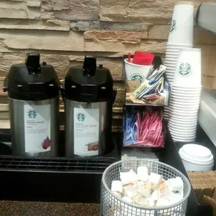 a coffee maker, two cups of coffee, a container of marshmallows, and a