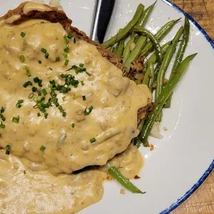Chicken fried steak with gravy and mashed potatoes underneath.  Green beans..