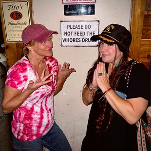 two women standing in front of a sign that says please do not feed the whores drug
