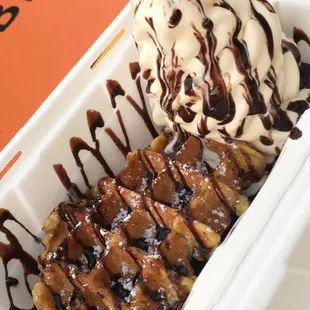 Belgium waffle with vanilla ice cream on the side with chocolate drizzle.