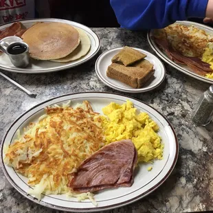 a breakfast of eggs, ham, hash browns, and pancakes