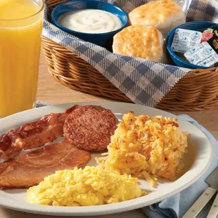 a plate of eggs, bacon, hash browns, biscuits, and a glass of orange juice