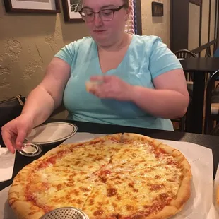 a woman sitting at a table with a large pizza