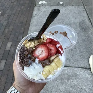 a hand holding a cup of fruit and yogurt