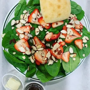 a plate of spinach salad with strawberries, almonds, and butter