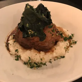 Lamb shank on a bed of mashed potatoes and topped with spinach.